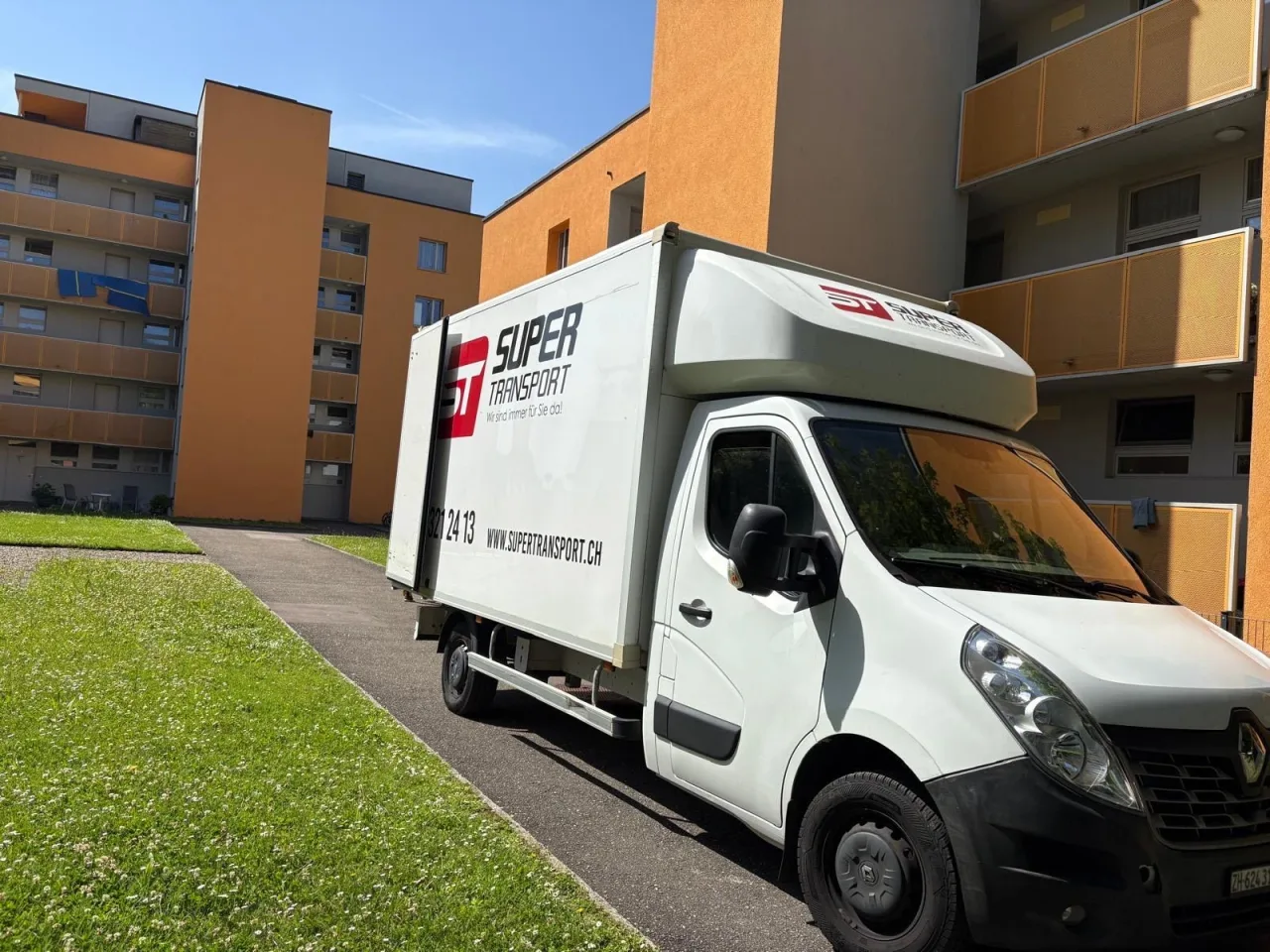 Umzugswagen von Super Transport vor Wohnblöcken mit orangen Balkonen