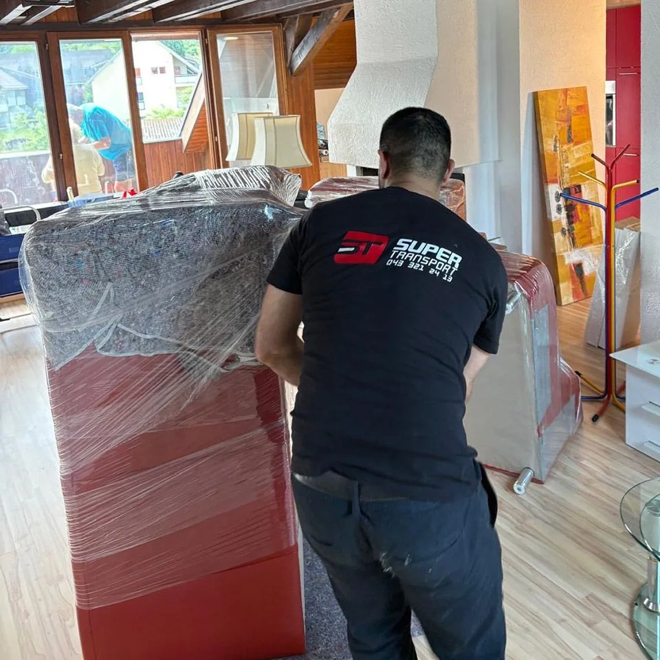 Mitarbeiter von Super Transport trägt ein eingefoliertes Polstermöbel durch eine Wohnung