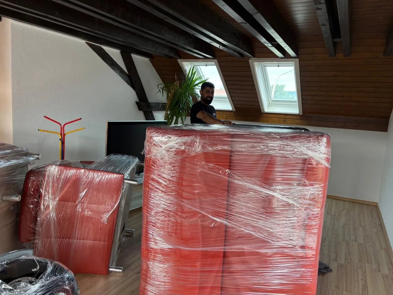 In Stretchfolie verpackte rote Stühle und Sessel in einem Büro unter dem Dach, bereit für den Transport