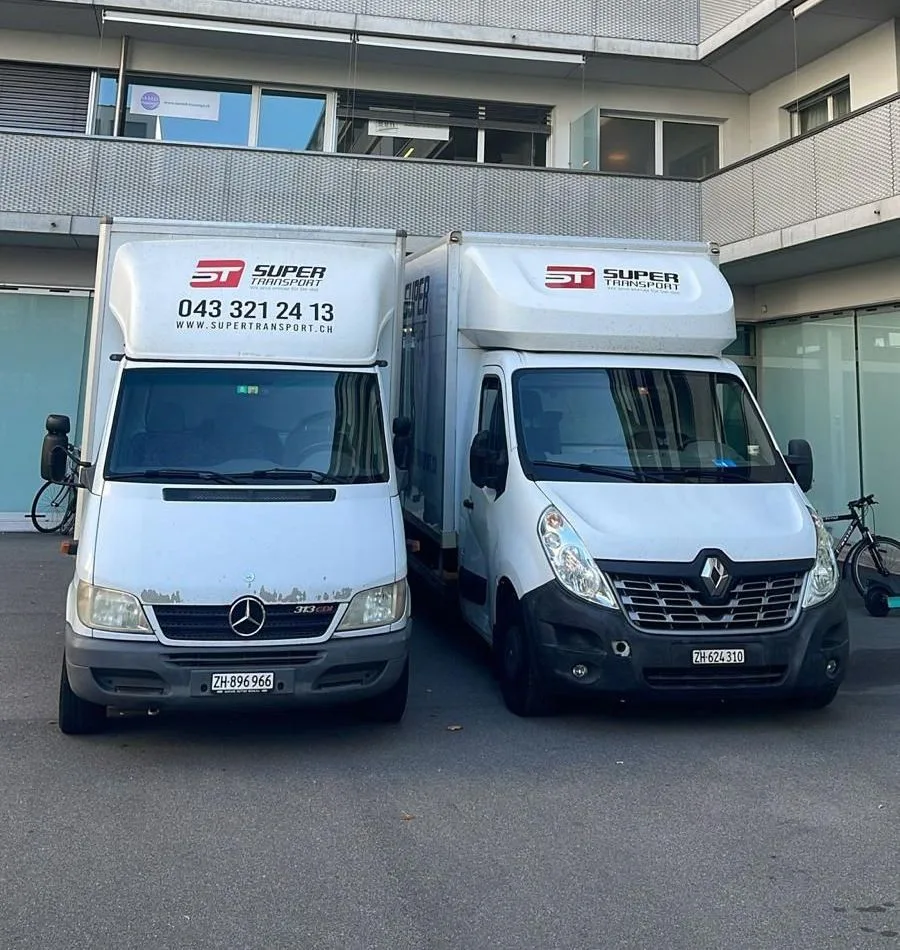 Two Super Transport removal trucks parked side by side in front of a modern building